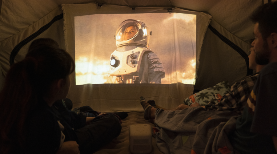 A group of friends watching a movie in a tent while camping out