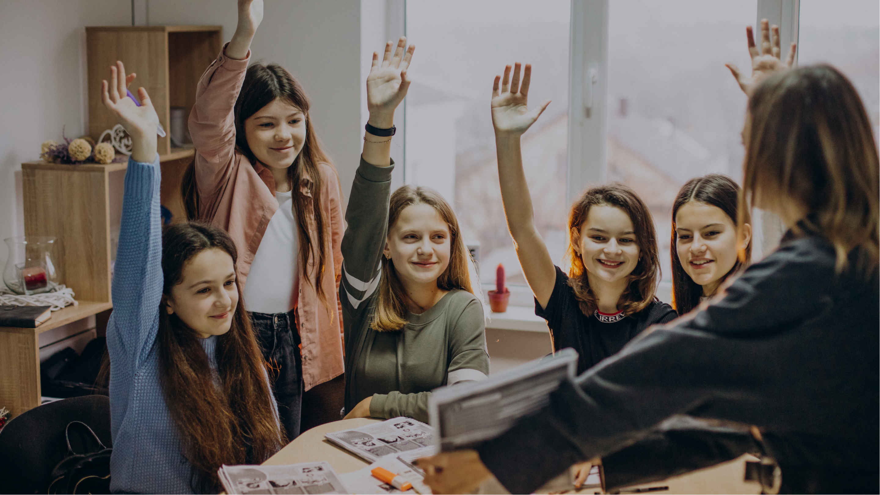 Students surrounding a teacher excitedly raising their hands to answer a question